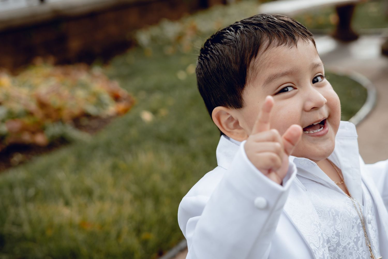 A young child in white formal attire smiles brightly during an outdoor event.