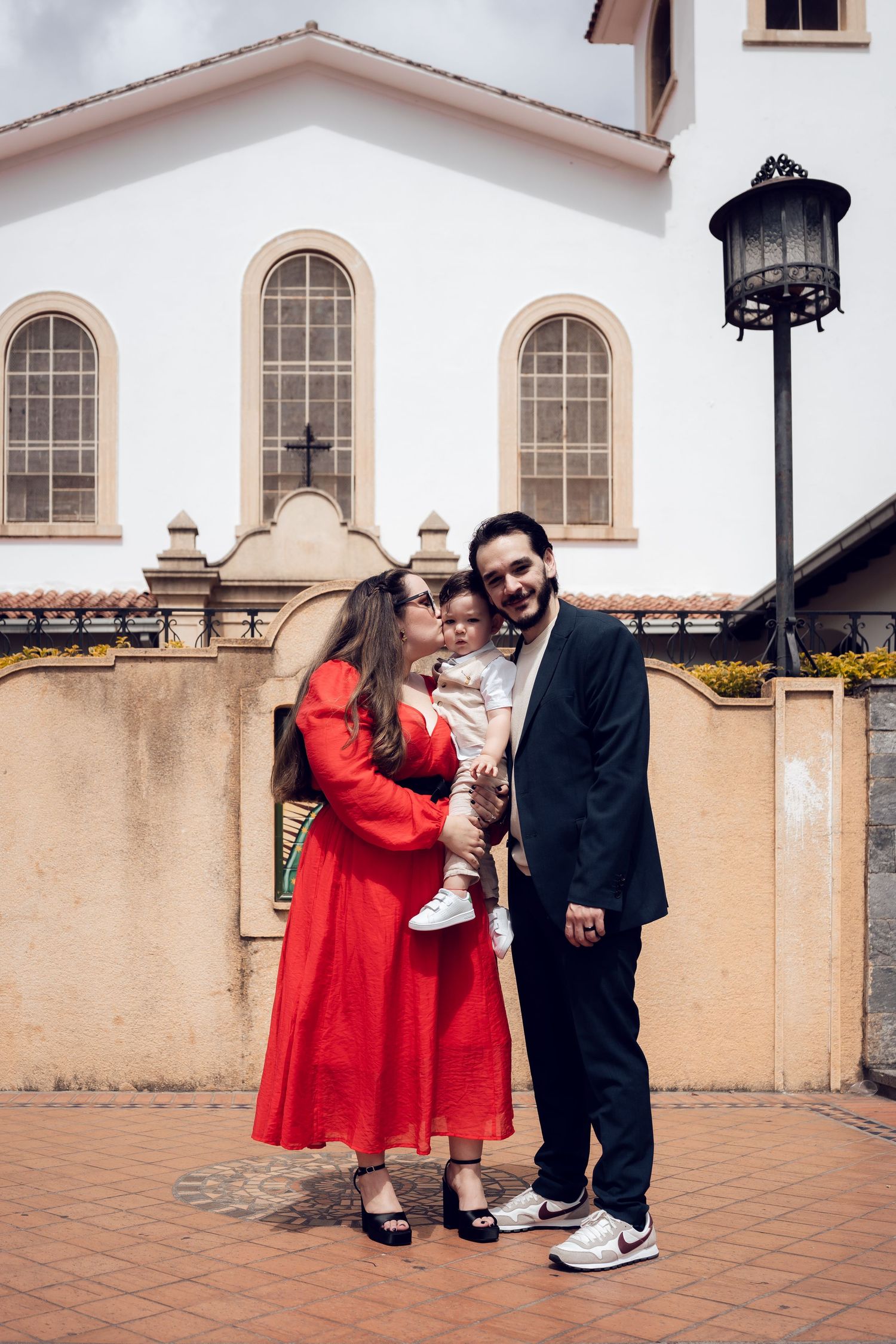 A family photo session outside a Spanish-style church building with arched windows and terra cotta roof.