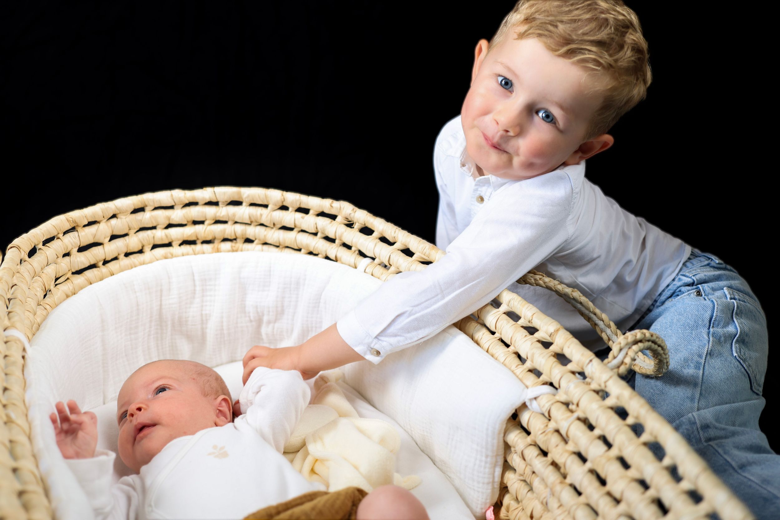 Petit garçon se penchant gentiment vers son petit frère allongé dans un couffin en osier.
Lumeria Photo Montfort sur meu