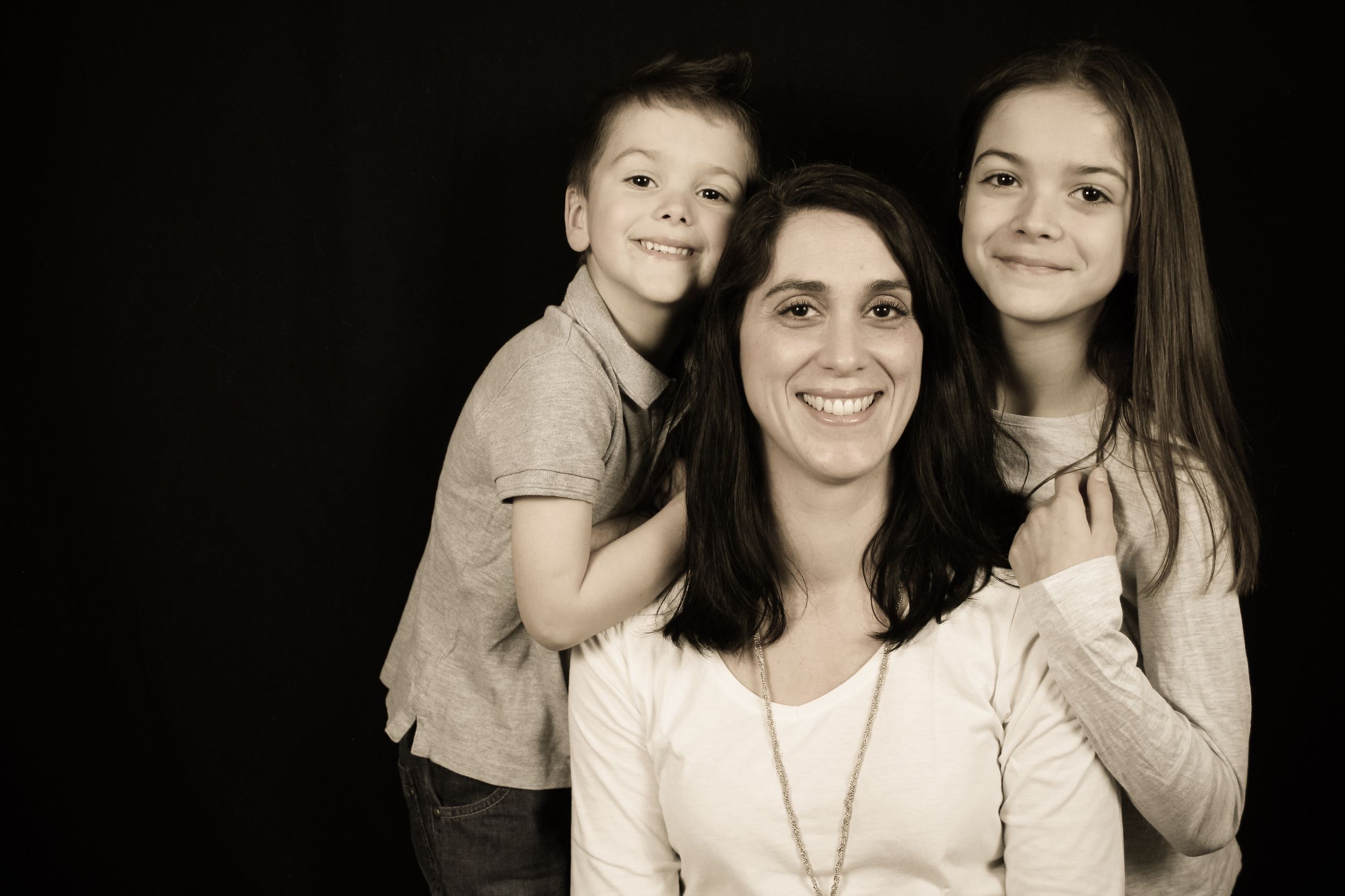Séance photo de famille en studio sur fond noir, portrait complice d'une maman avec ses deux enfants.
Lumeria Photo Montfort sur meu