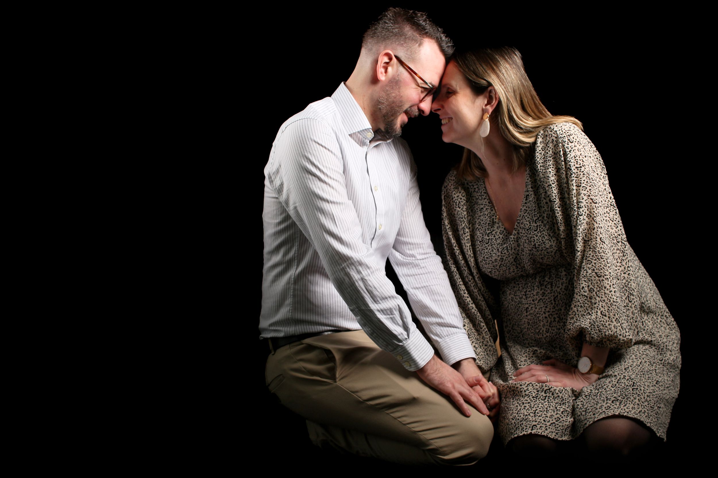 Portrait de couple attendant un enfant lors d'une séance photo grossesse studio, regard complice fond noir.
Lumeria Photo Montfort sur meu