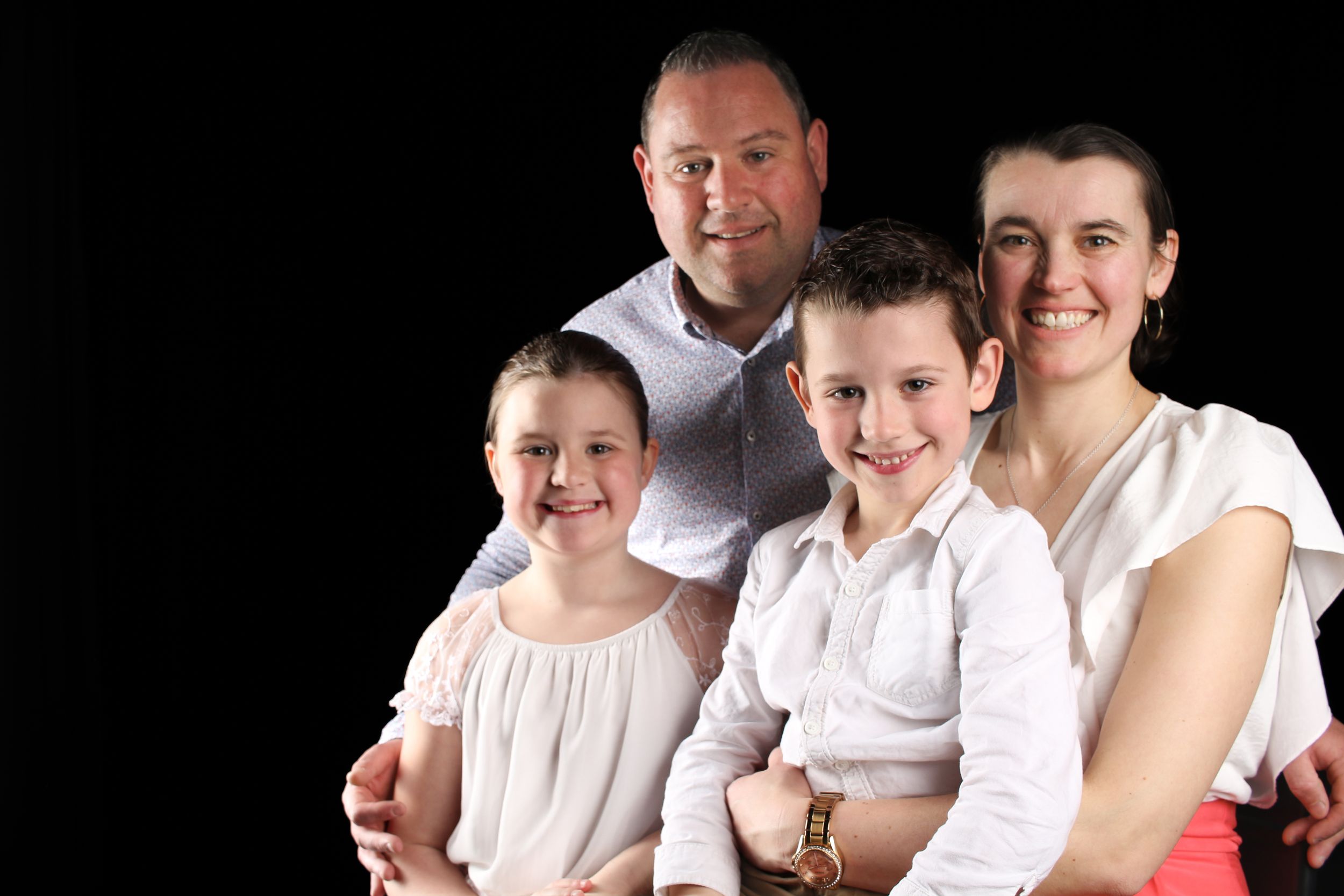 Portrait de famille studio, parents et enfants posant ensemble en vêtements clairs sur fond noir.
Lumeria Photo Montfort sur meu