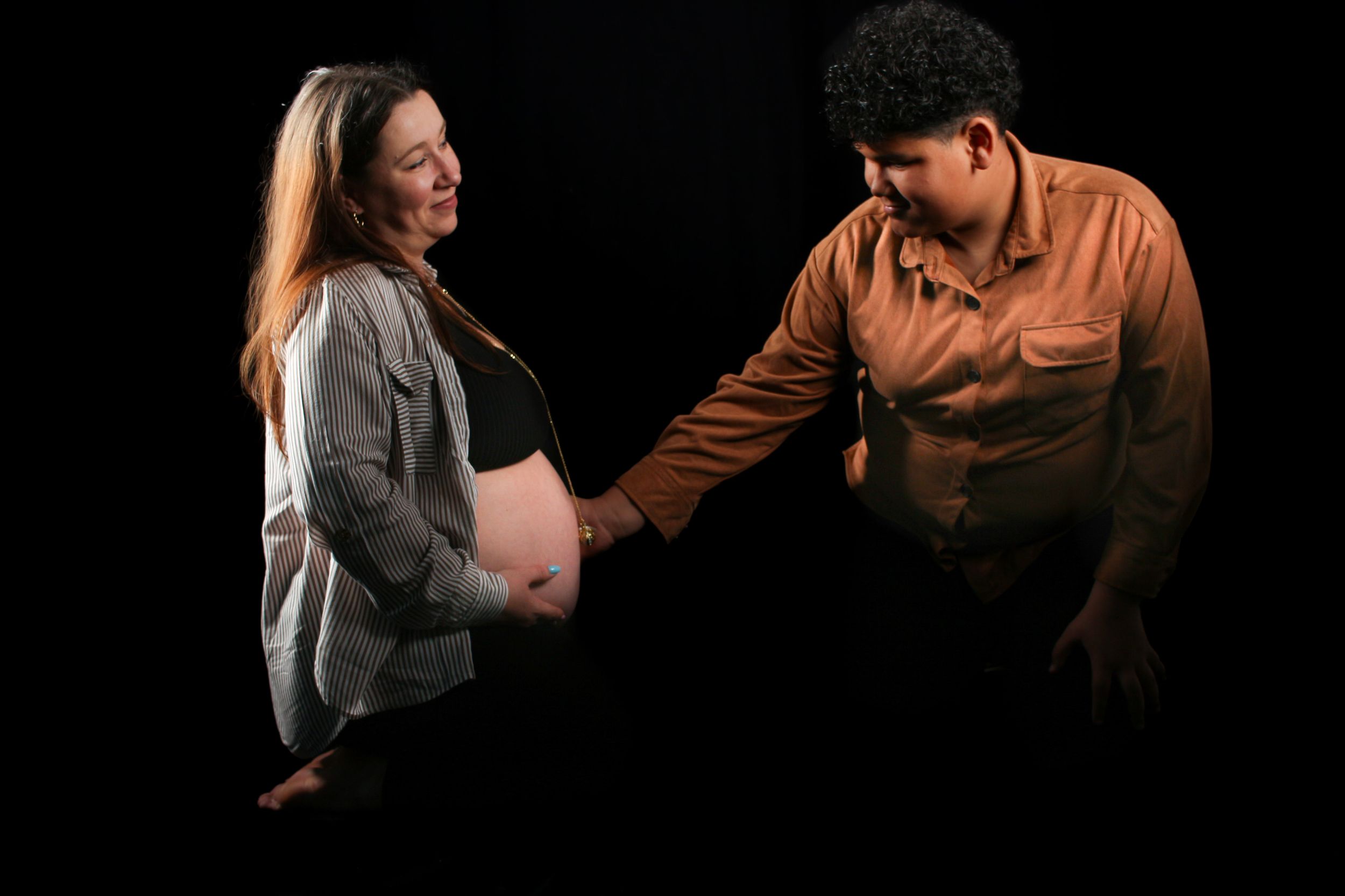 Shooting photo grossesse studio, futur maman avec le grand frère posant sur fond noir mettant en valeur le ventre rond de la maman.