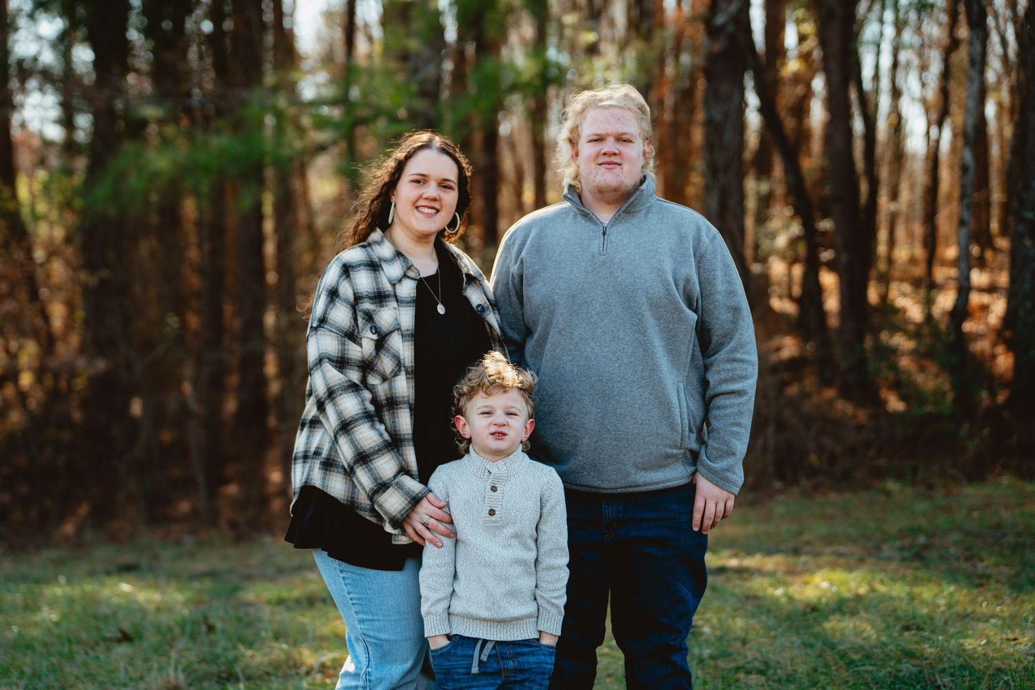 Family enjoying a casual outdoor photo session in a sunlit forest setting.