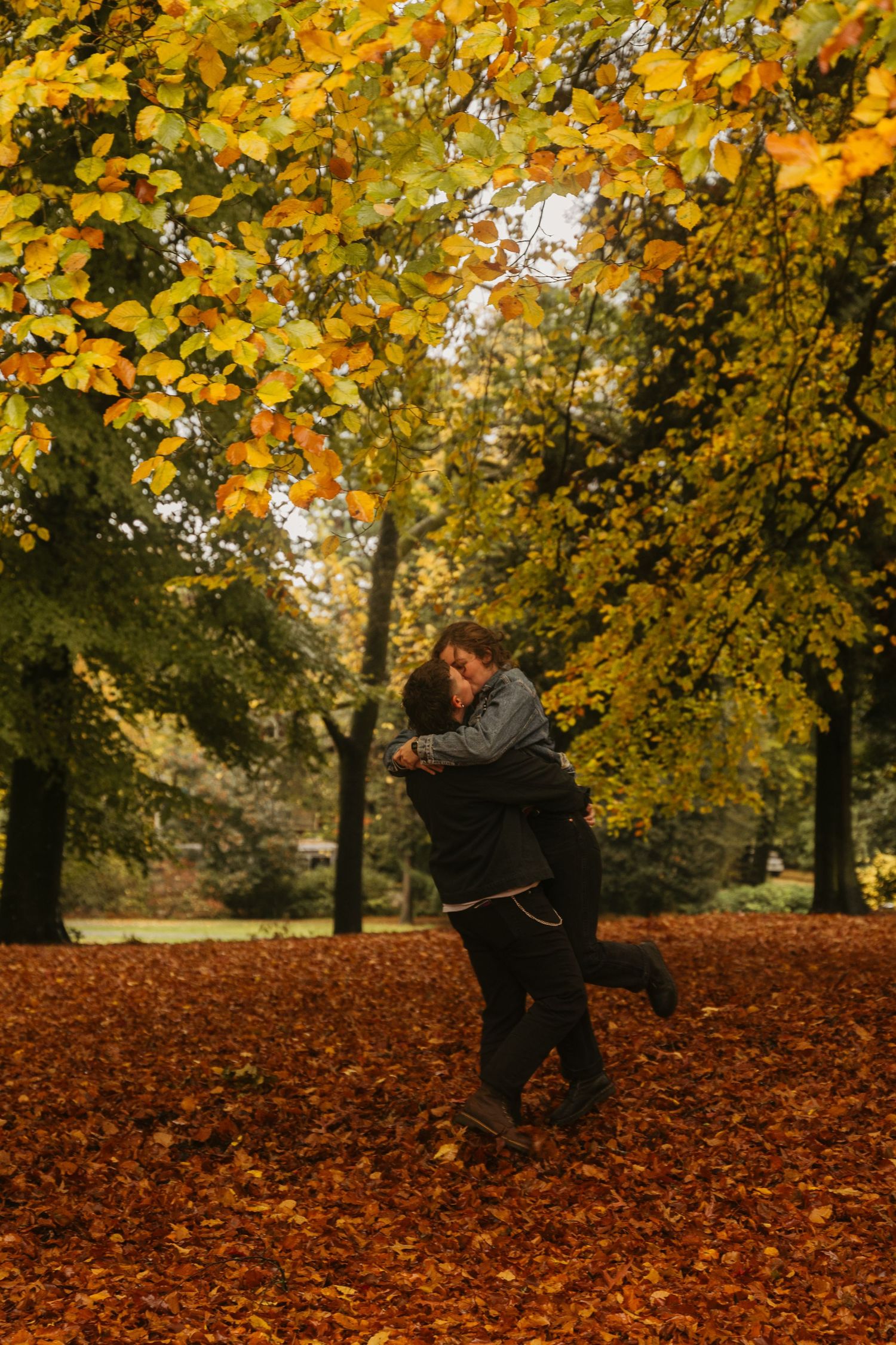Person walking through vibrant autumn leaves in park with golden foliage overhead creating scenic fall atmosphere.