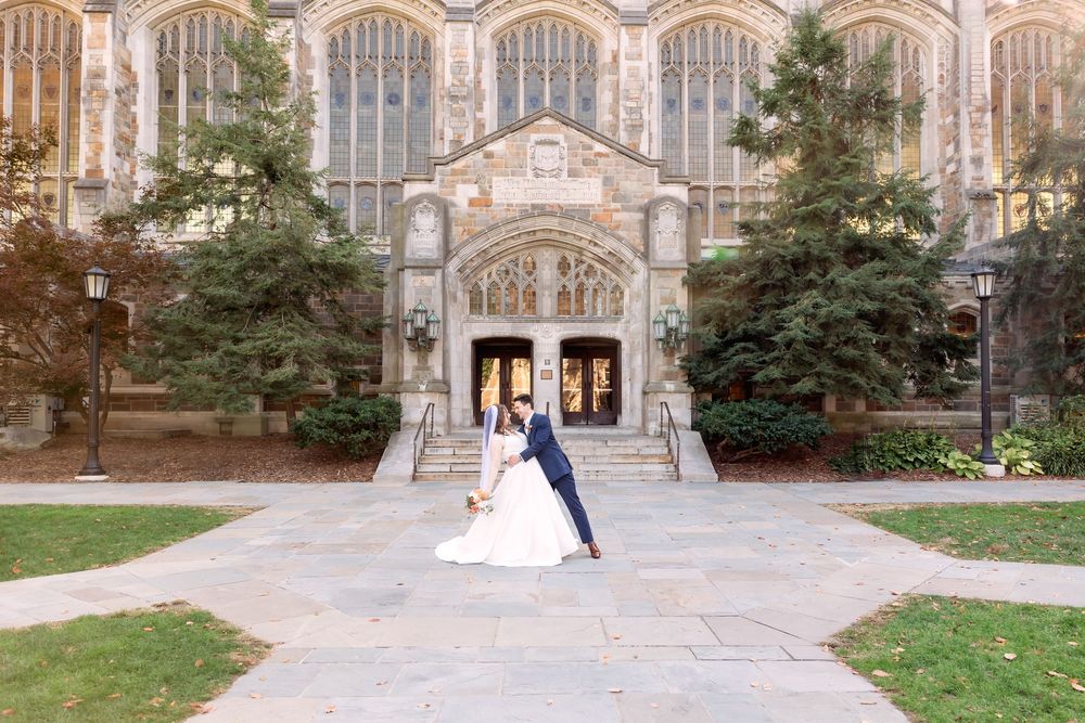 Elegant couple poses for wedding photos in front of a grand Gothic stone church entrance on a sunny autumn day.