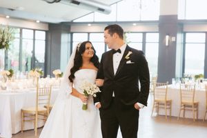 A wedding couple shares an intimate moment during their first dance in an elegant reception venue with large windows.