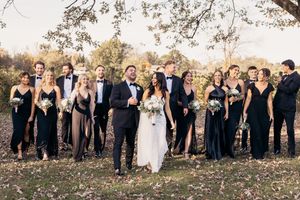 Wedding party in formal black and white attire poses together outdoors during autumn season.