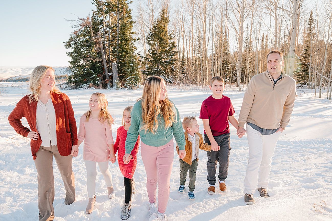 A group walks together holding hands in a snowy winter landscape with evergreen trees in the background.