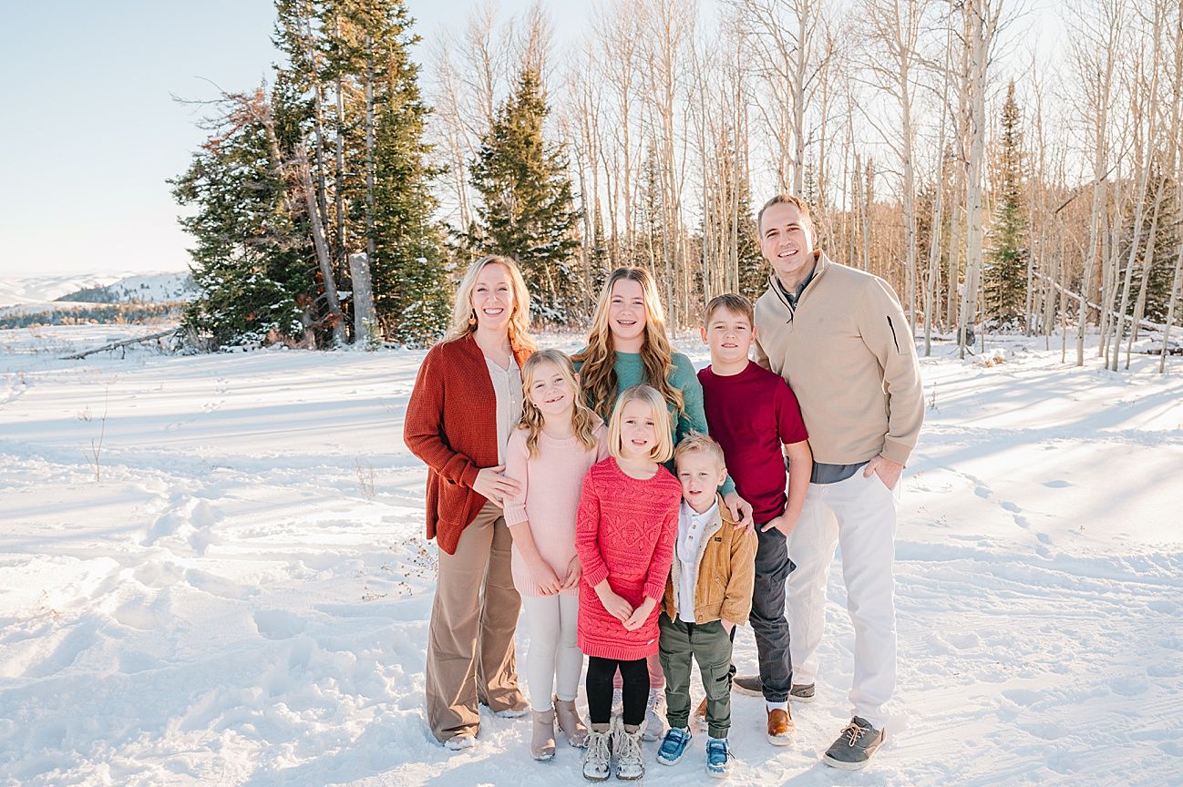 Winter family portrait with group standing together in snowy landscape surrounded by evergreen and birch trees.