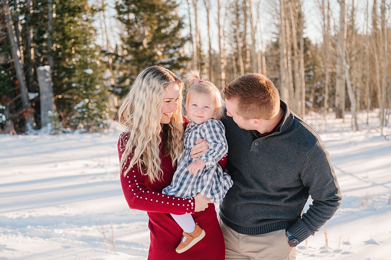 A family shares a tender moment together in a snowy forest setting during winter.