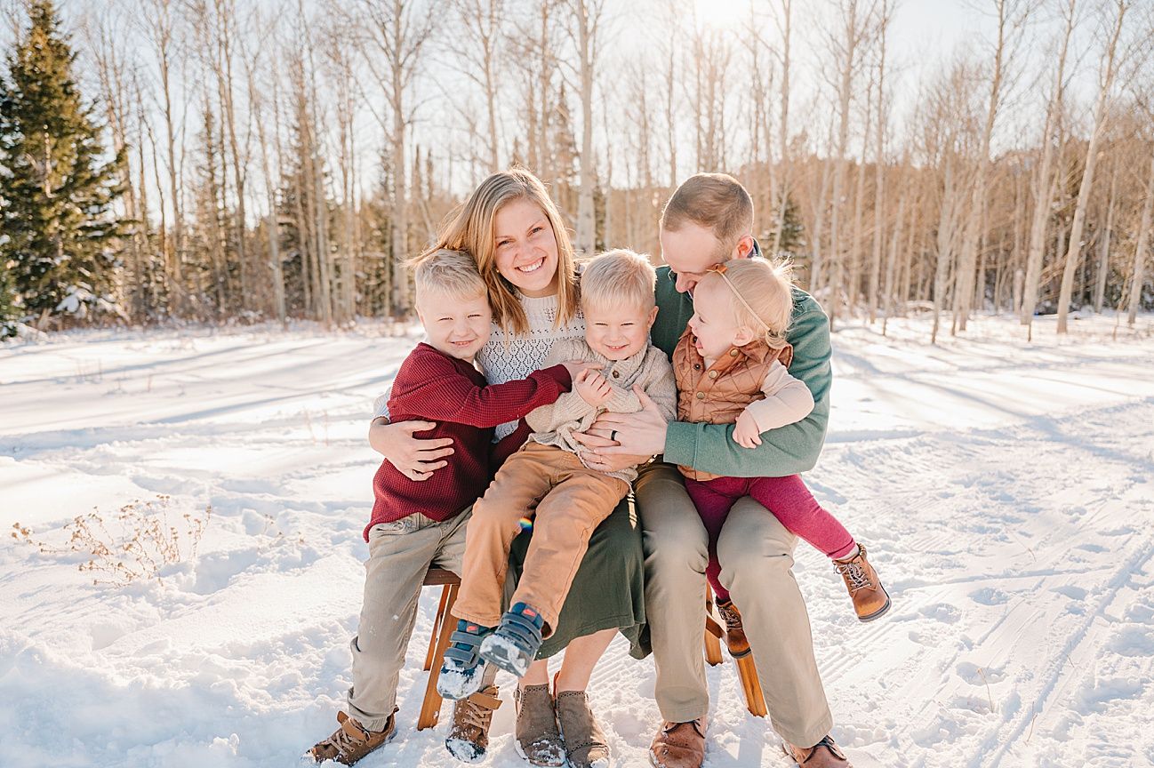 Family sitting together on a snowy ground surrounded by winter trees.