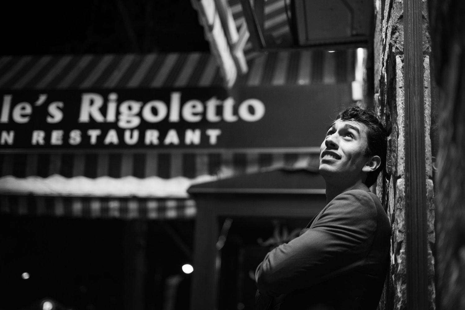 A black and white street scene shows someone performing on a stage with dramatic lighting and shadows.