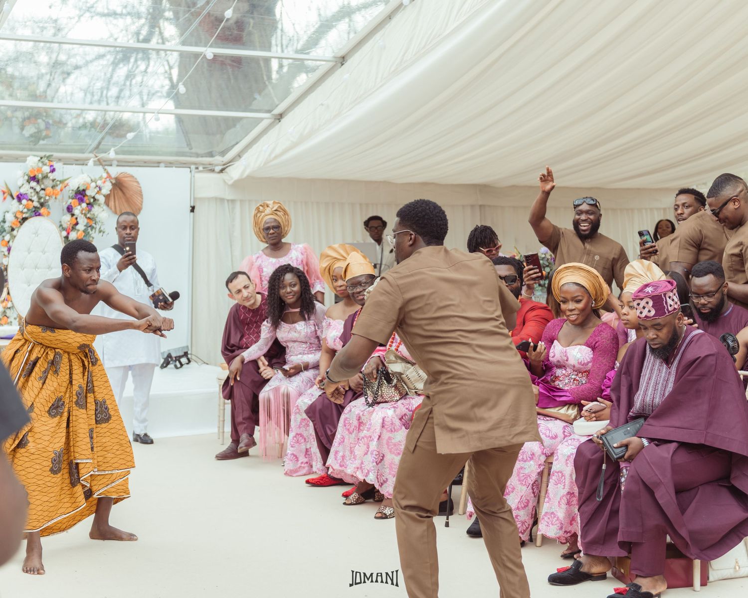 Traditional African wedding ceremony with energetic dancers performing before seated guests in colorful attire.
