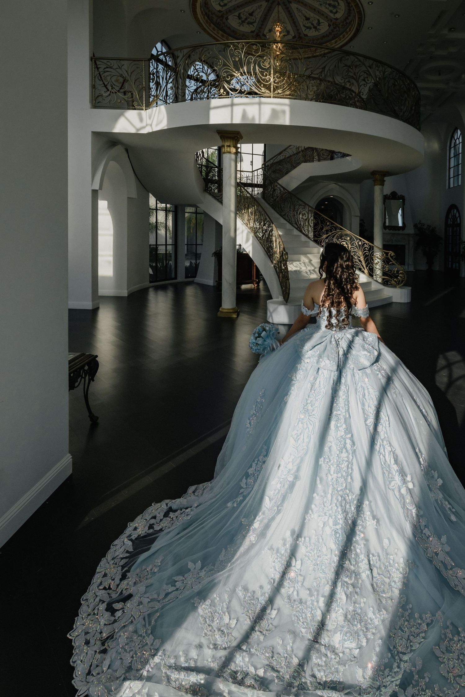 A stunning white ball gown with intricate lace details photographed in an elegant interior with a spiral staircase.