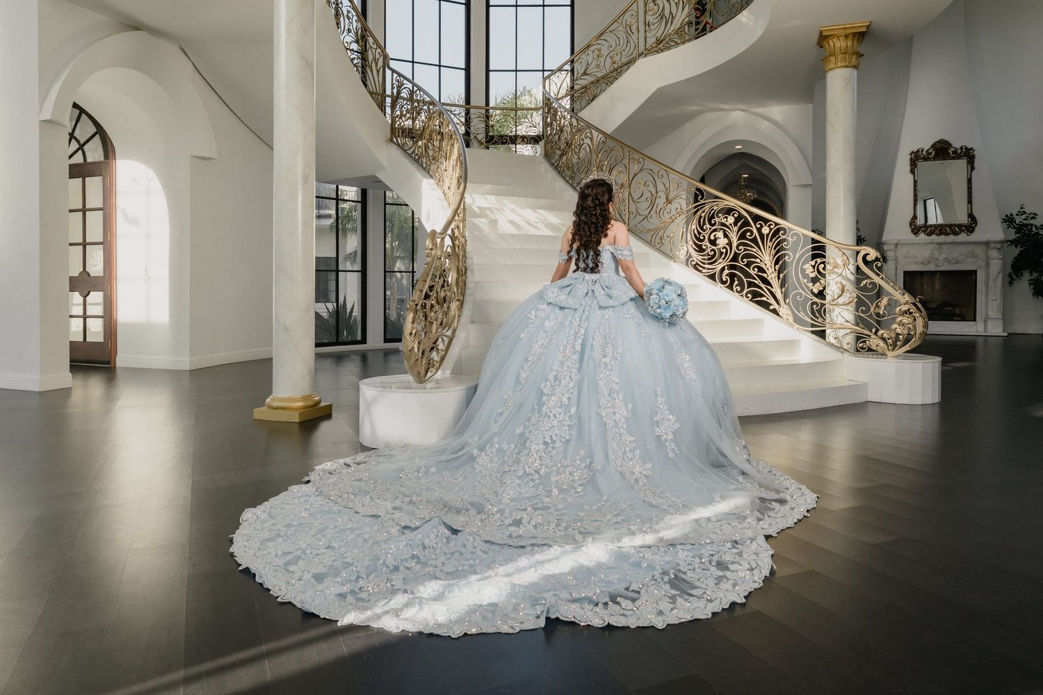 An ethereal blue ballgown with long train photographed on an elegant curved staircase with ornate gold railings.