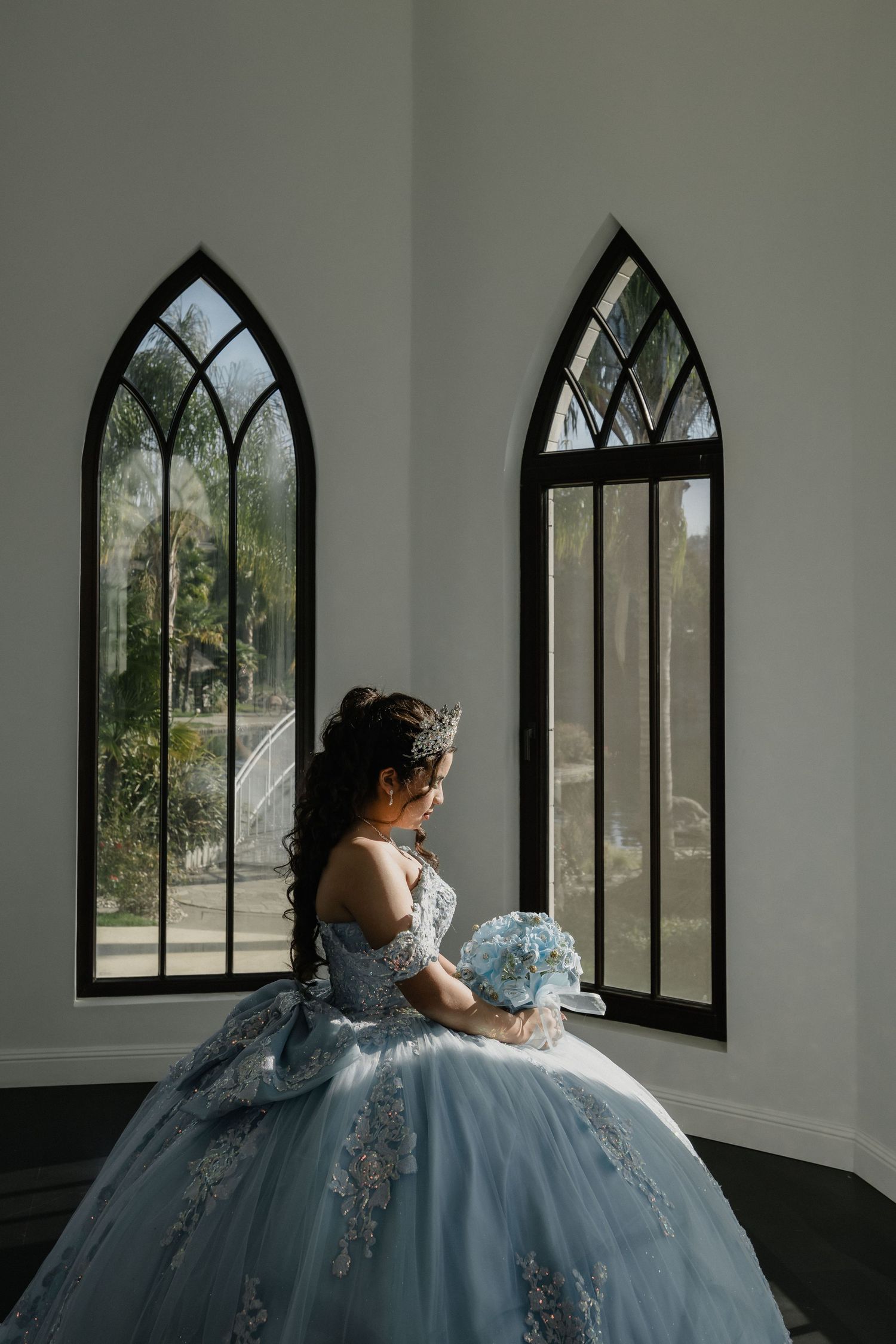 Elegant ball gown with light blue details photographed through gothic arched windows in a bright interior space.