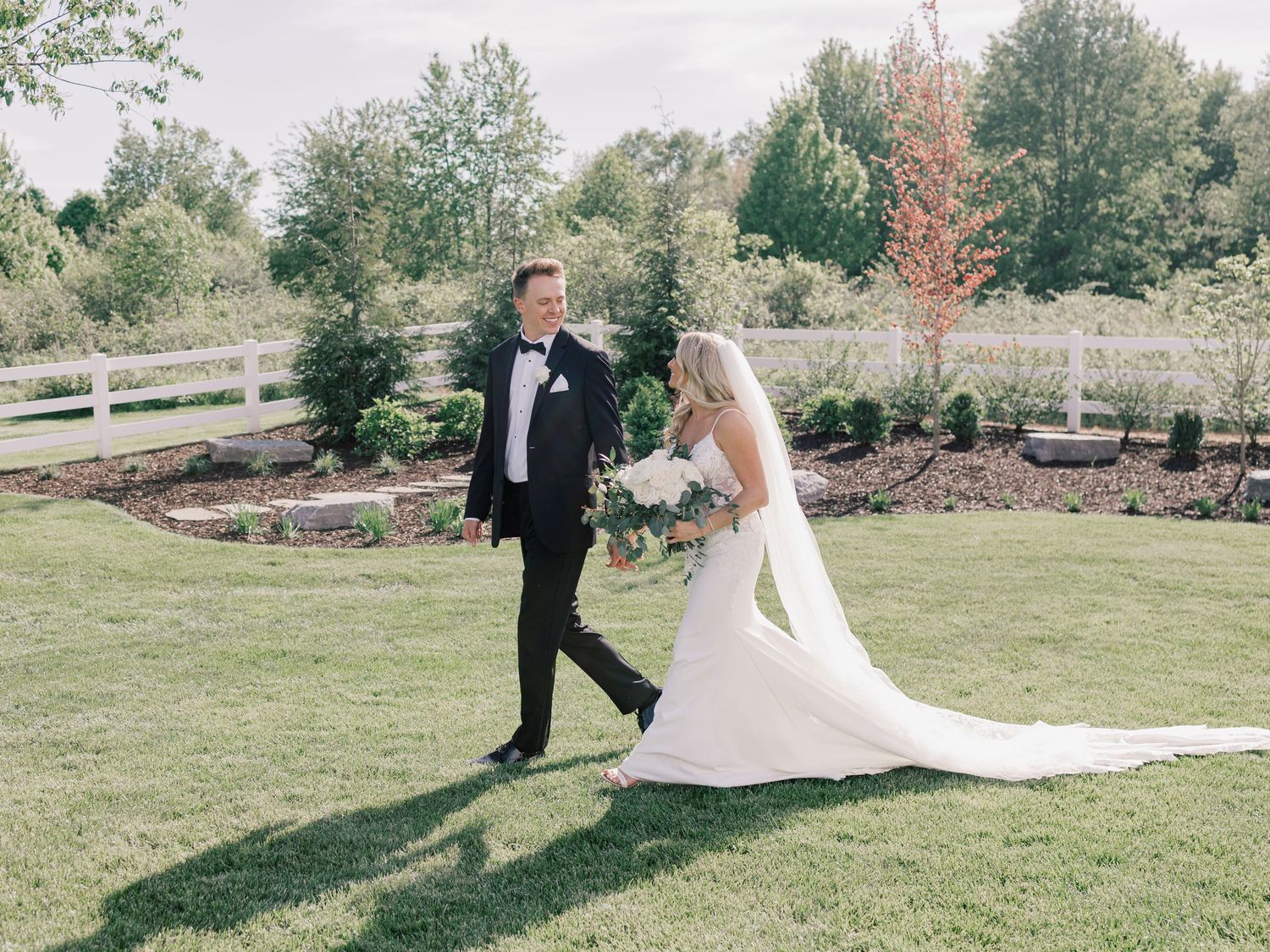 A couple in wedding attire walks across a scenic green lawn during their outdoor celebration.