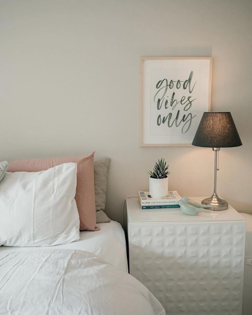 Minimalist bedroom decor with white bedding, pink accents, and wall art featuring inspirational text in soft tones.
