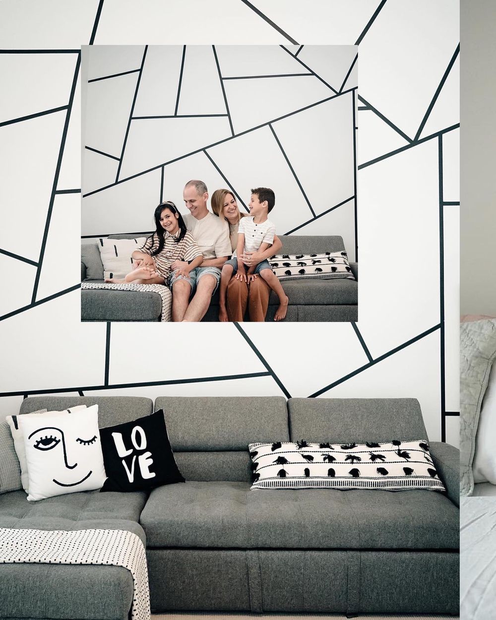 Modern living room with gray sectional sofa against geometric black and white patterned wall featuring decorative pillows.