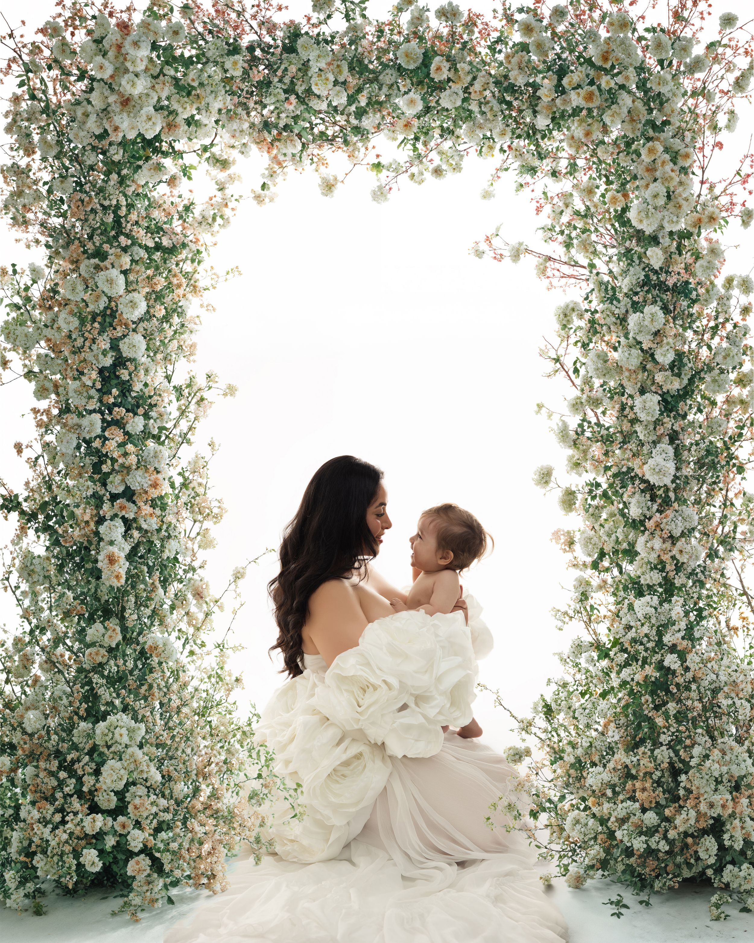 An elegant portrait under a lush white floral arch with delicate baby's breath and roses against a light backdrop.