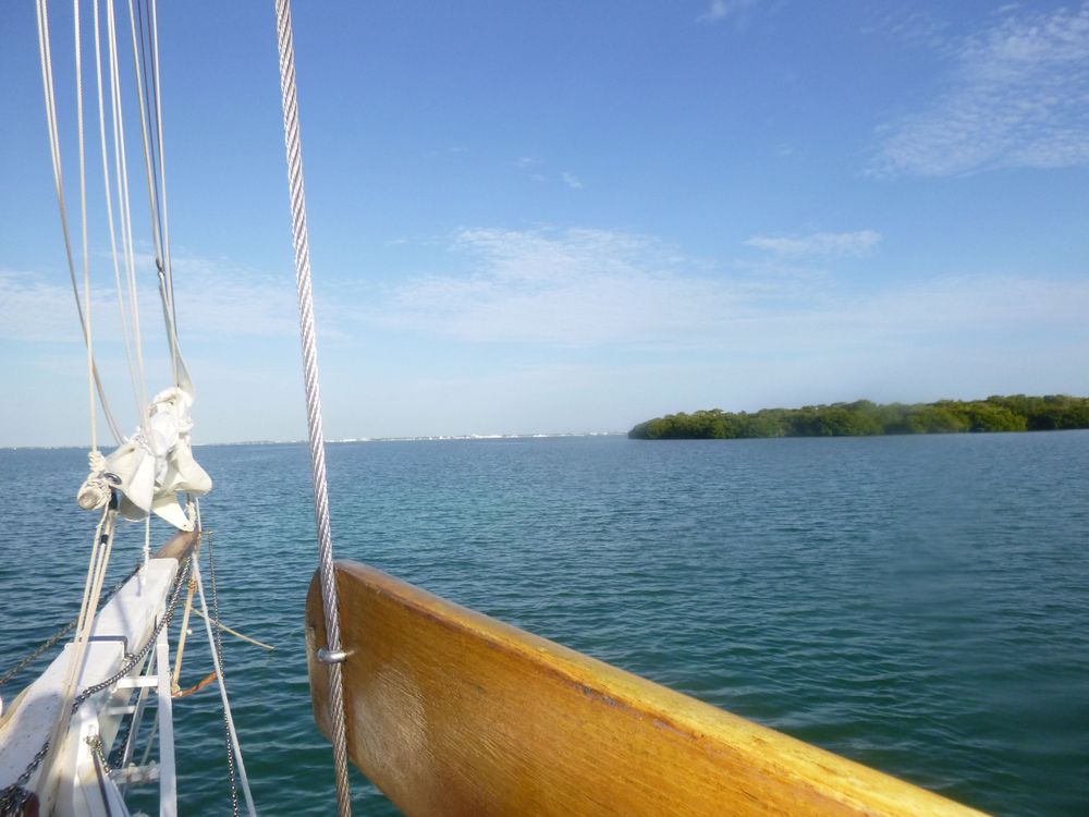 A peaceful sailing scene unfolds with a view from the deck toward a small, tree‑covered island.