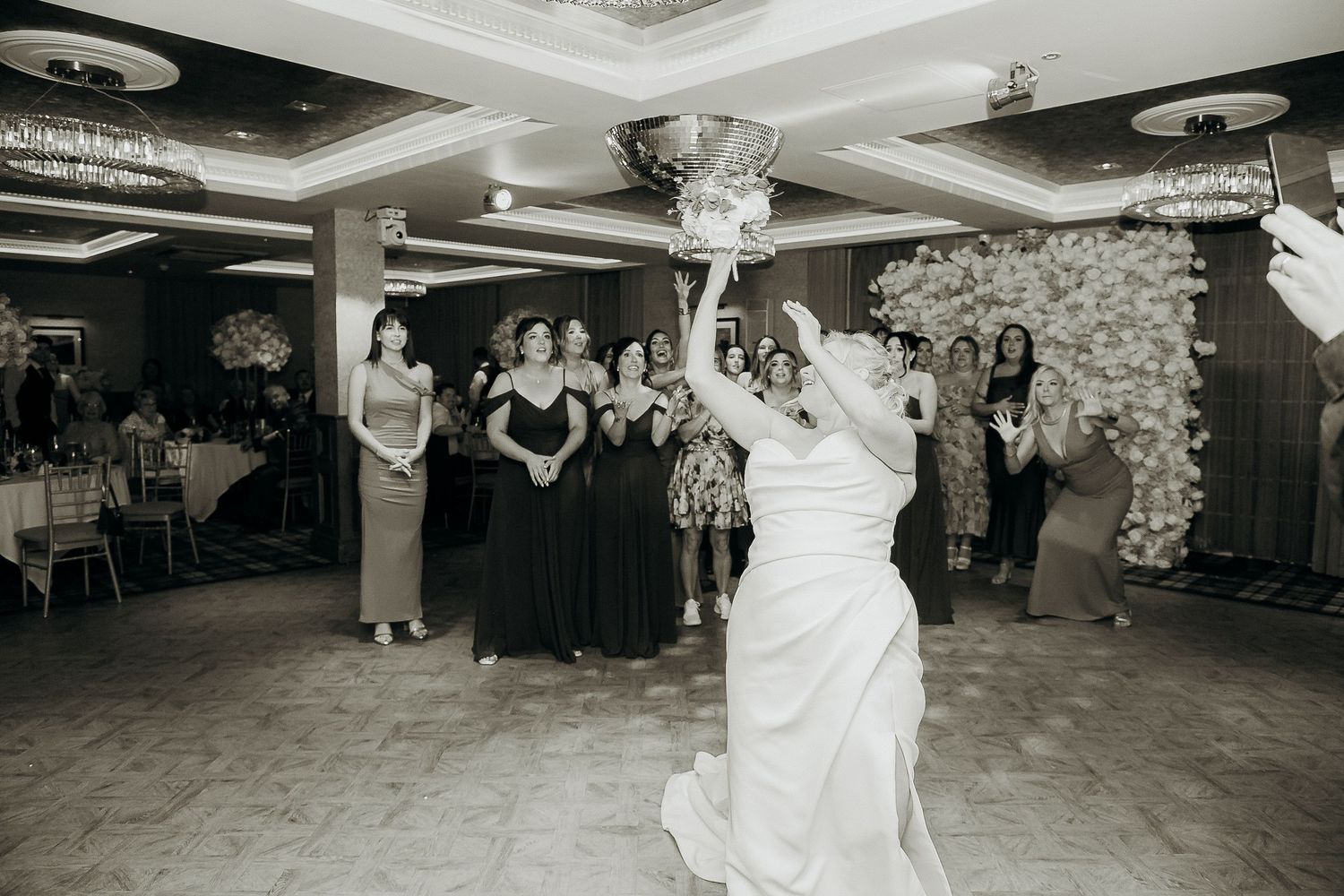 Wedding guests dance and celebrate on an elegant ballroom floor under crystal chandeliers.