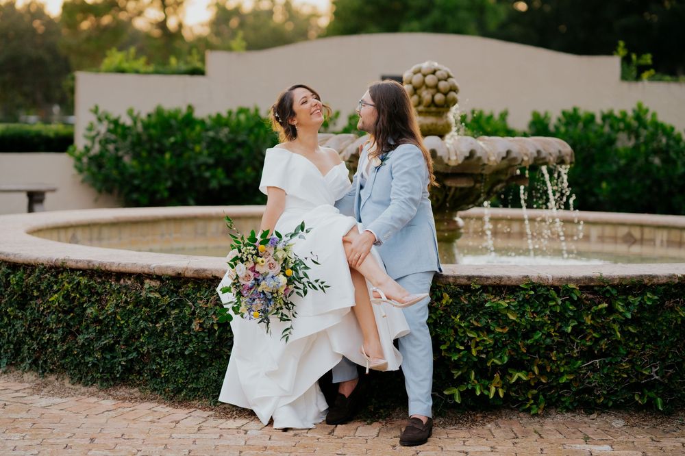 Happy couple shares a romantic moment by an outdoor fountain at sunset during their wedding celebration.