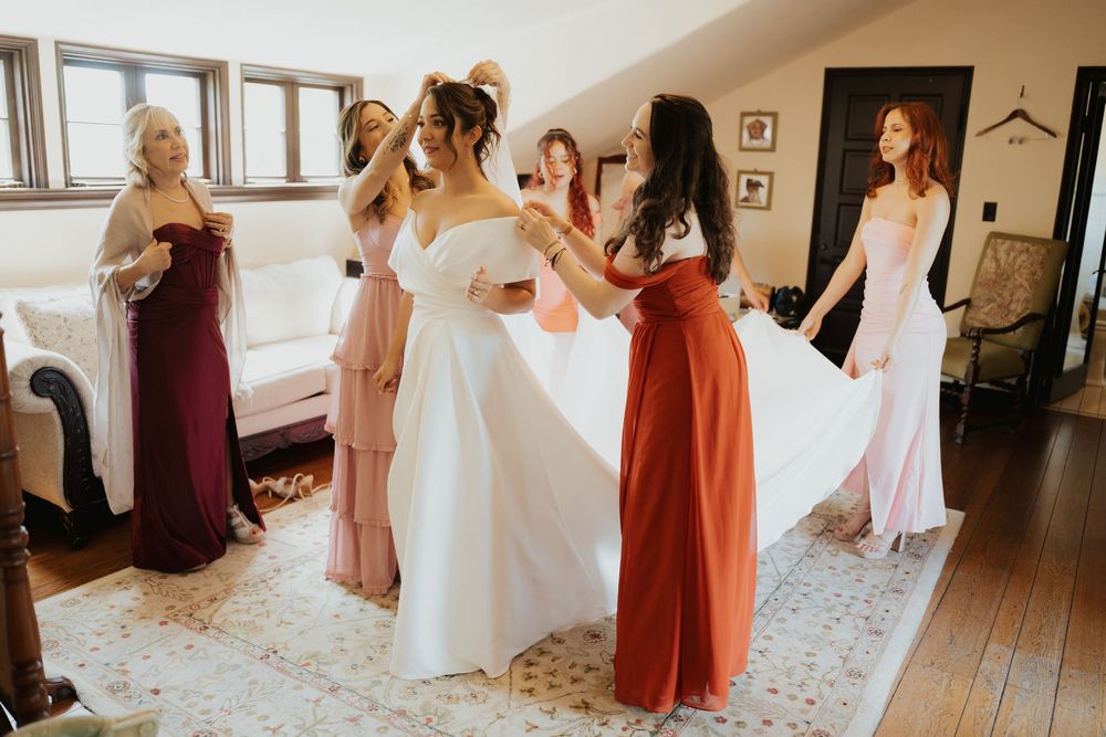 A group of women in pastel dresses gather in a room during wedding preparations.