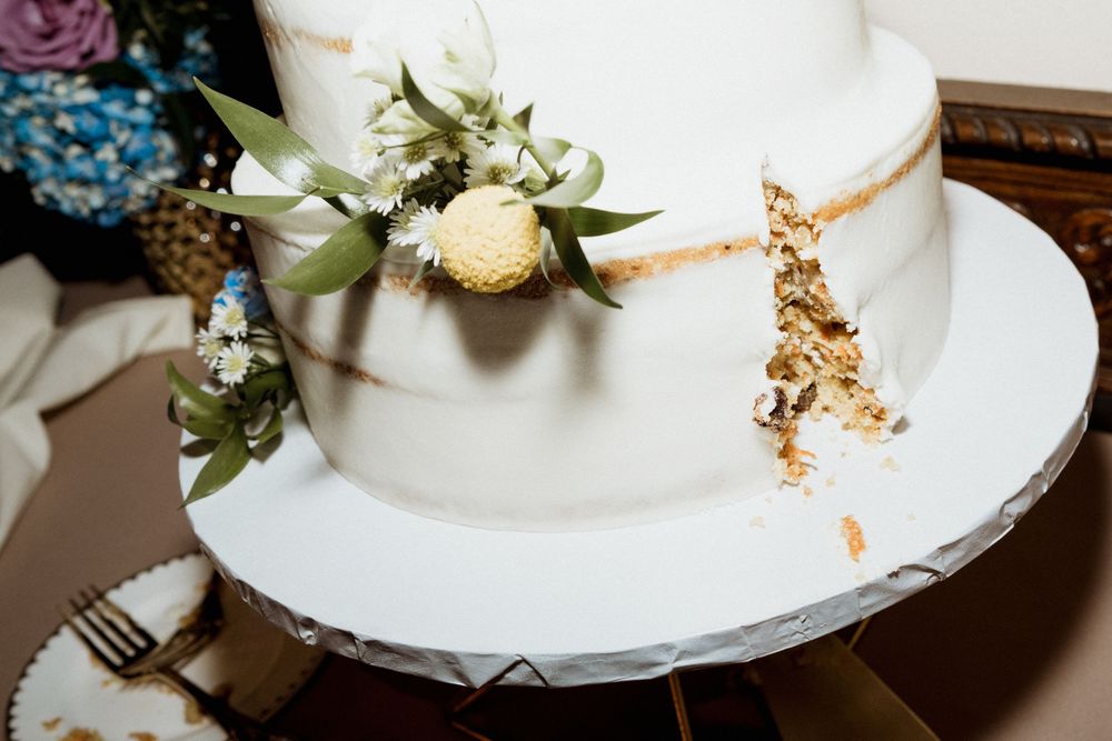 Close-up view of a white wedding cake decorated with delicate flowers and gold accents on a white cake stand.