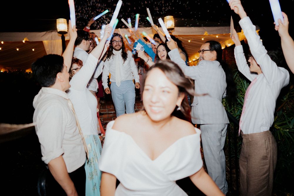 Wedding guests dance and celebrate with raised arms at a nighttime outdoor reception.