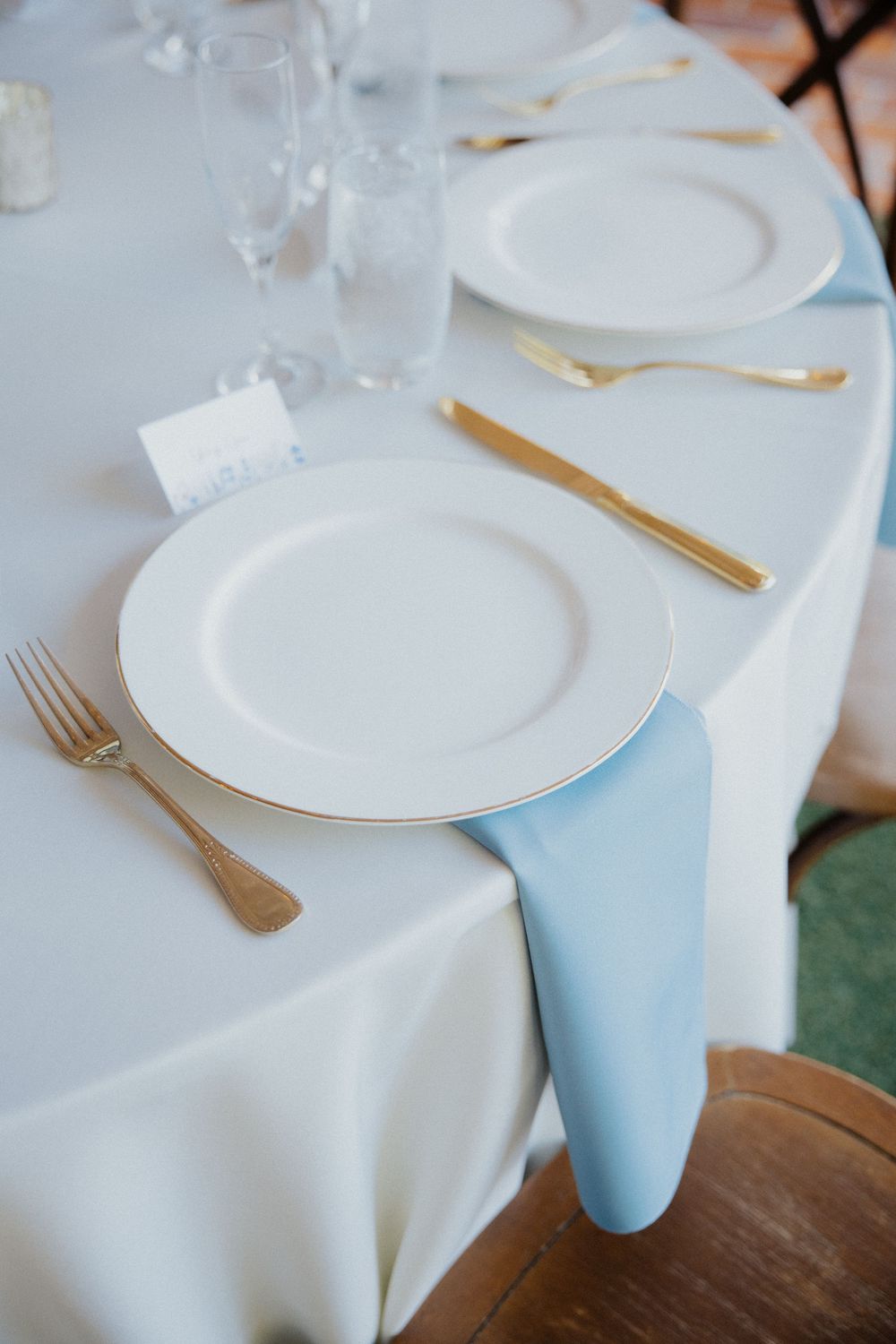 Elegant table setting with white plates, gold cutlery, and light blue napkins.