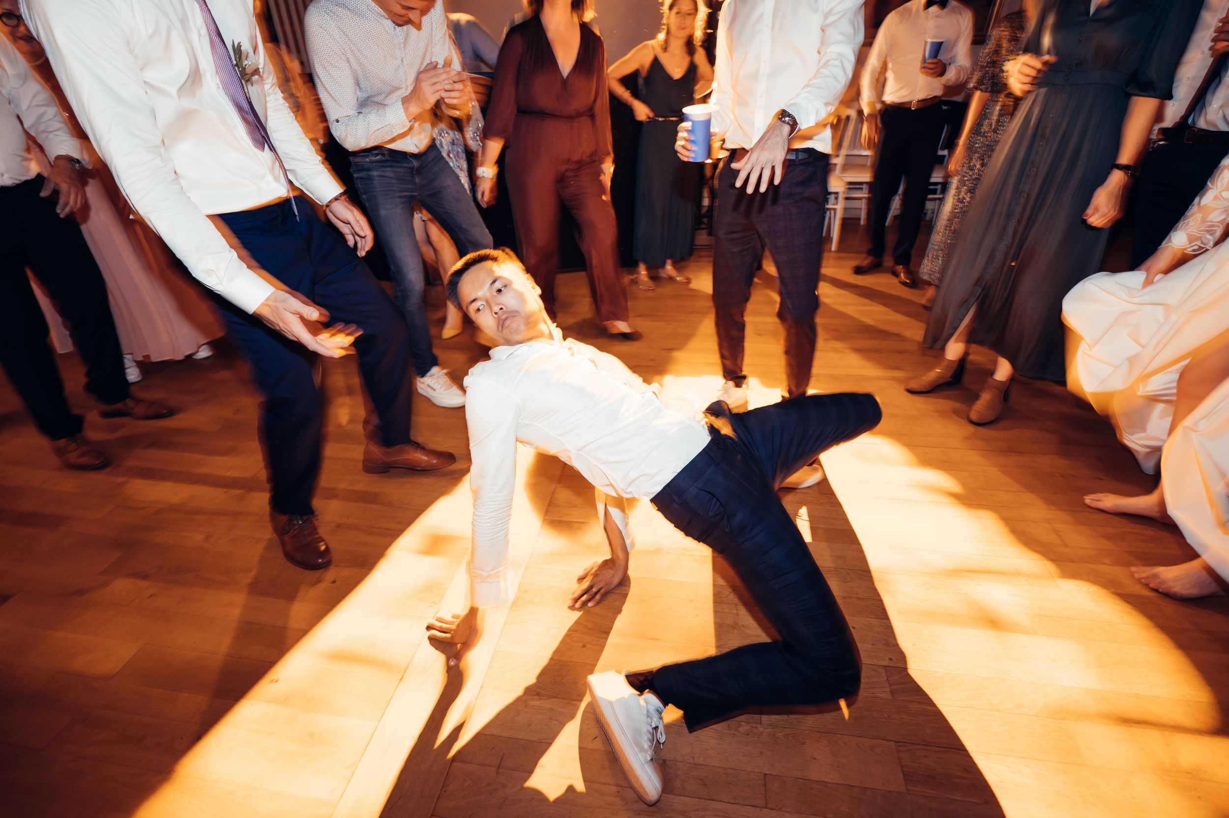 Invité réalisant une figure de danse au centre de la piste lors d’une réception de mariage animée.
