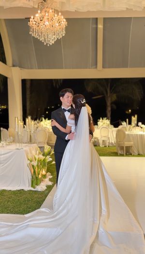 Bride and groom share first dance under crystal chandelier at elegant outdoor wedding reception with white decor.