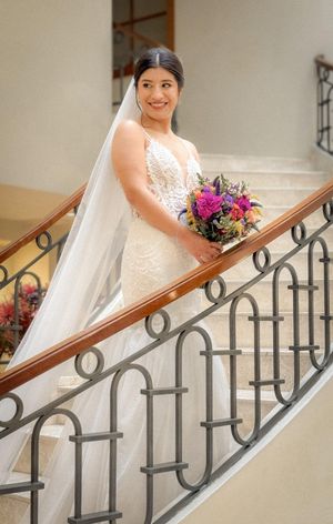 Wedding scene on an elegant staircase with wrought iron railings and colorful floral bouquet.
