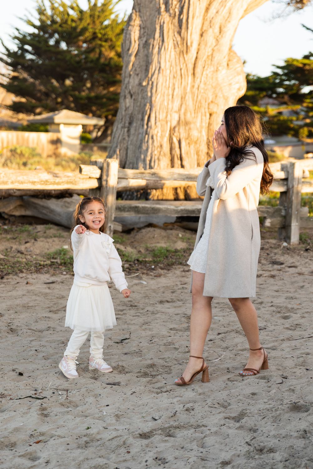 White dress and shoes walking on sandy beach near a large tree trunk.