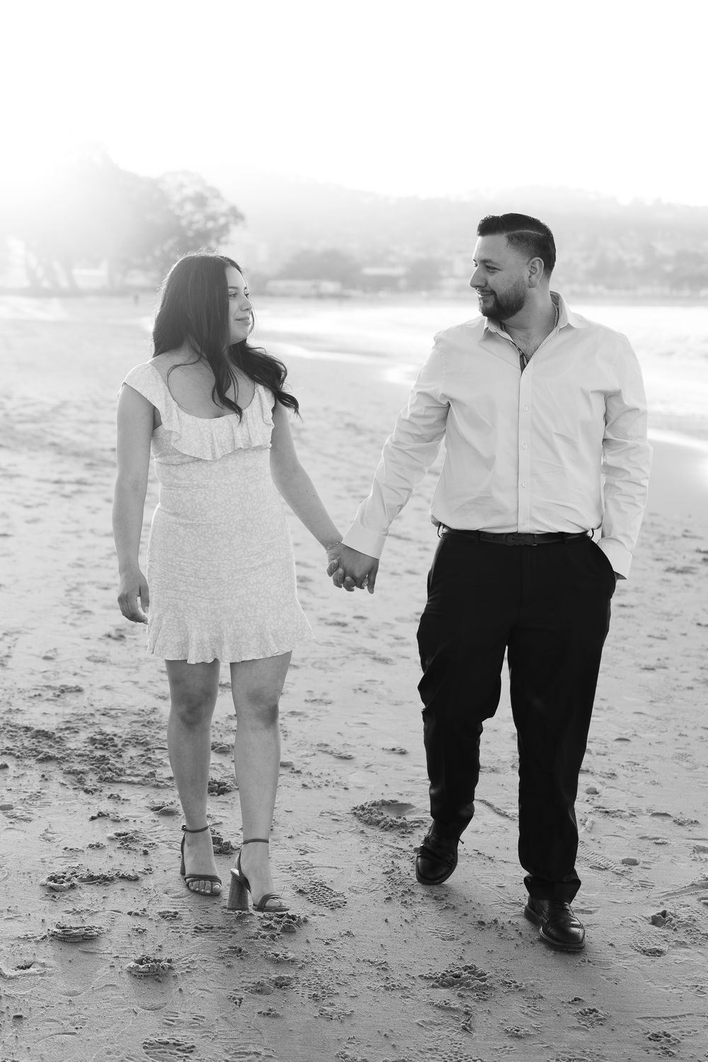 A couple walking together on a sandy beach, captured in black and white photography.
