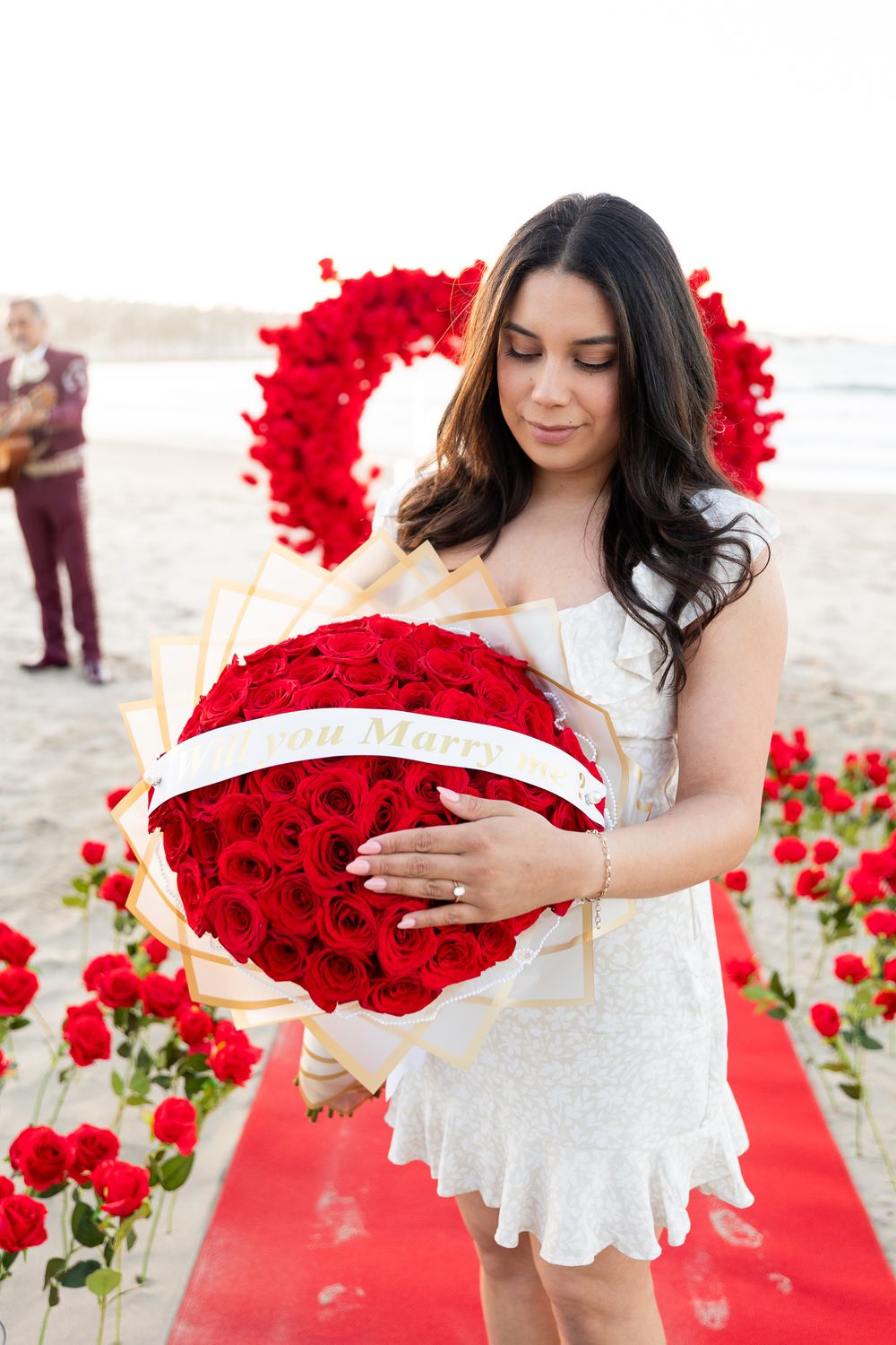 White dress against vibrant red roses arranged on a beach setting at sunset.