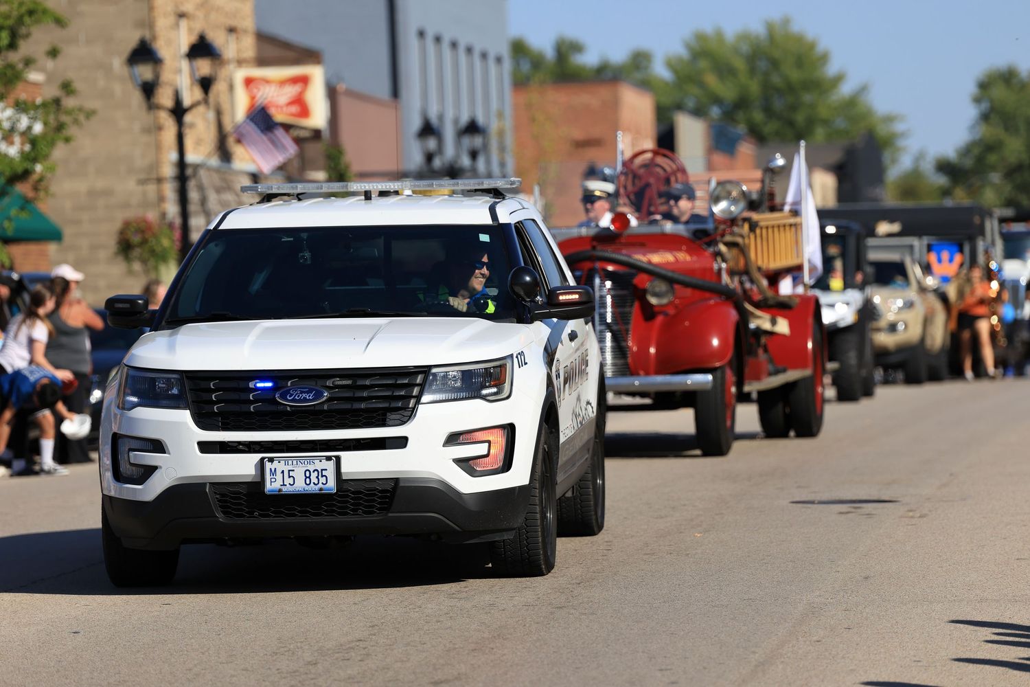 Police vehicle and red antique car lead a parade down a small town street.