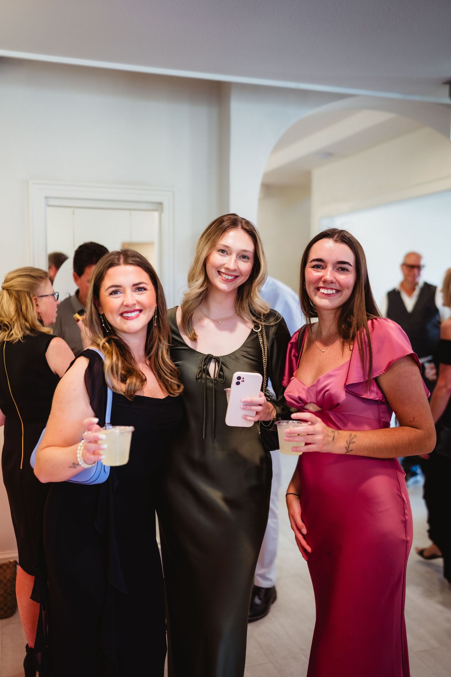 A group of people in formal attire gather together at an indoor event, wearing black and burgundy dresses.