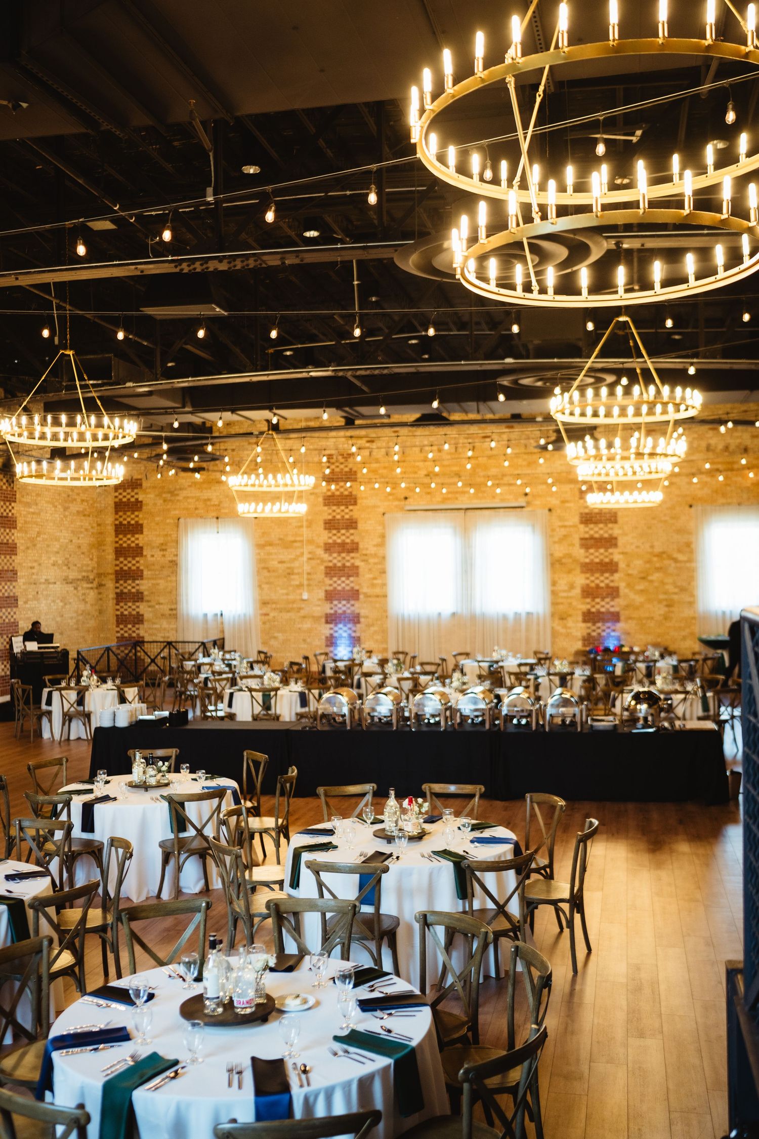 Elegant wedding reception venue with circular chandeliers, exposed brick walls, and tables set with white linens.
