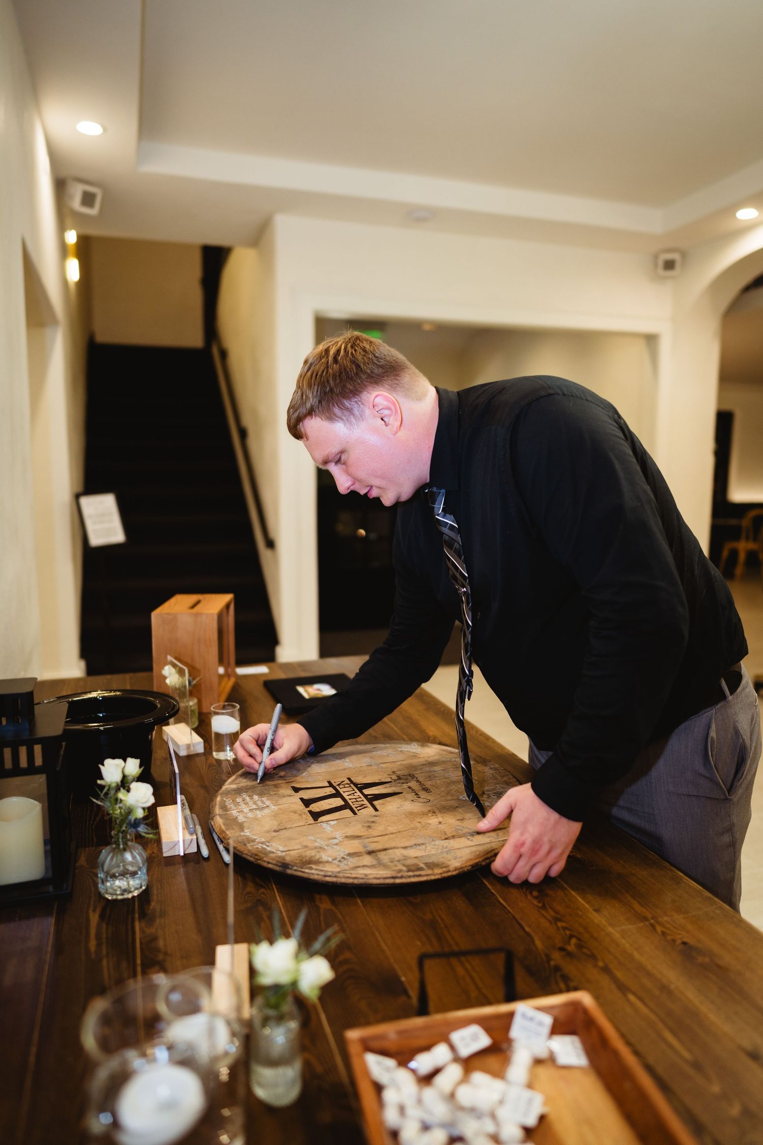 A sequence of photos showing someone signing a wooden guest book table at an indoor venue.