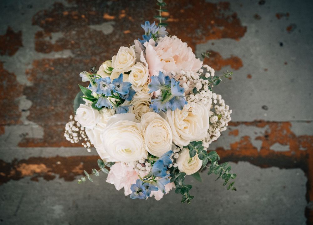 Romantic wedding bouquet with blush roses, blue hydrangeas and delicate greenery against textured background.