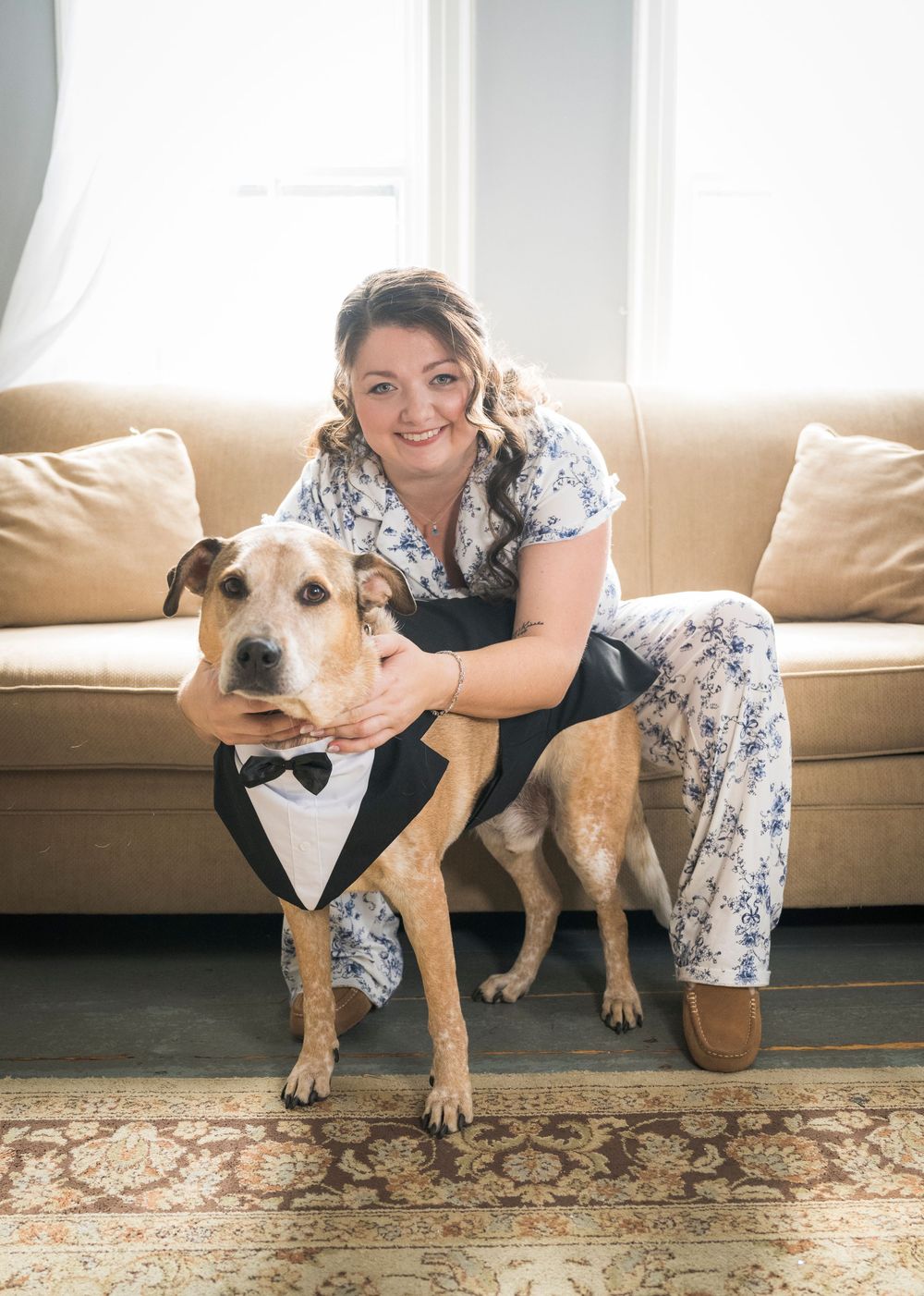A dog wearing a bow tie poses with someone on a couch during wedding preparations.
