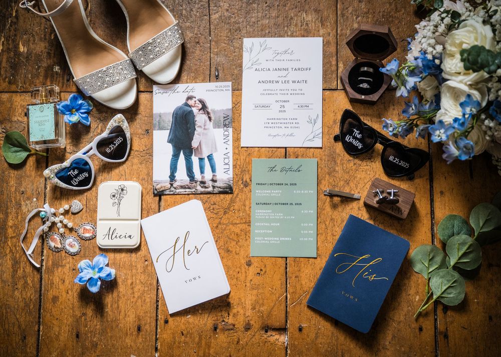 Wedding details flatlay with invitations, shoes, flowers and rings on wooden surface.