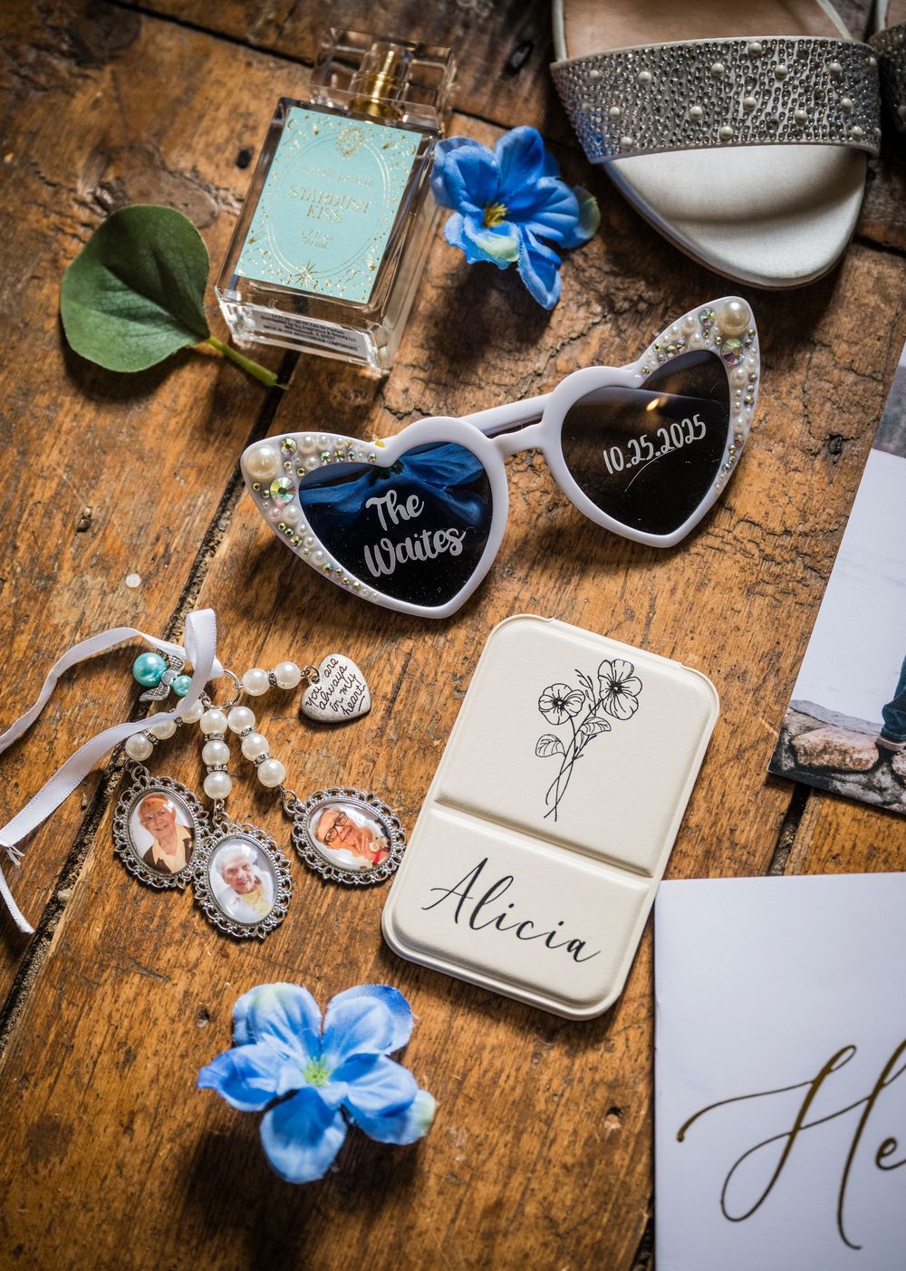 Wedding accessories and stationery arranged on rustic wooden surface including blue ribbons and calligraphy details.