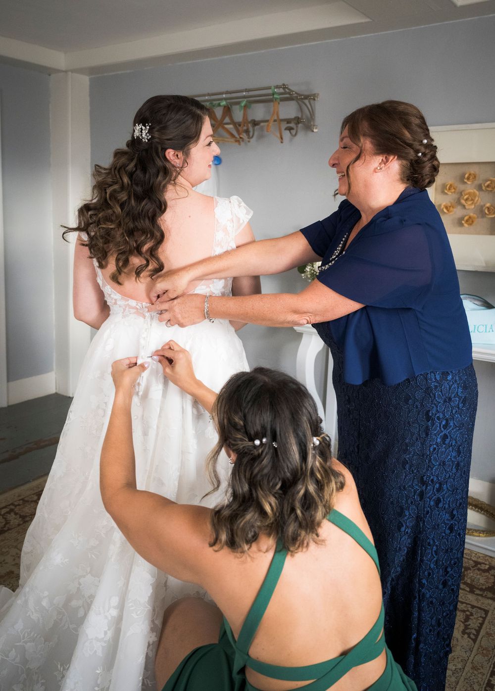 Wedding dress preparations with attendants helping with final adjustments in a bright room.
