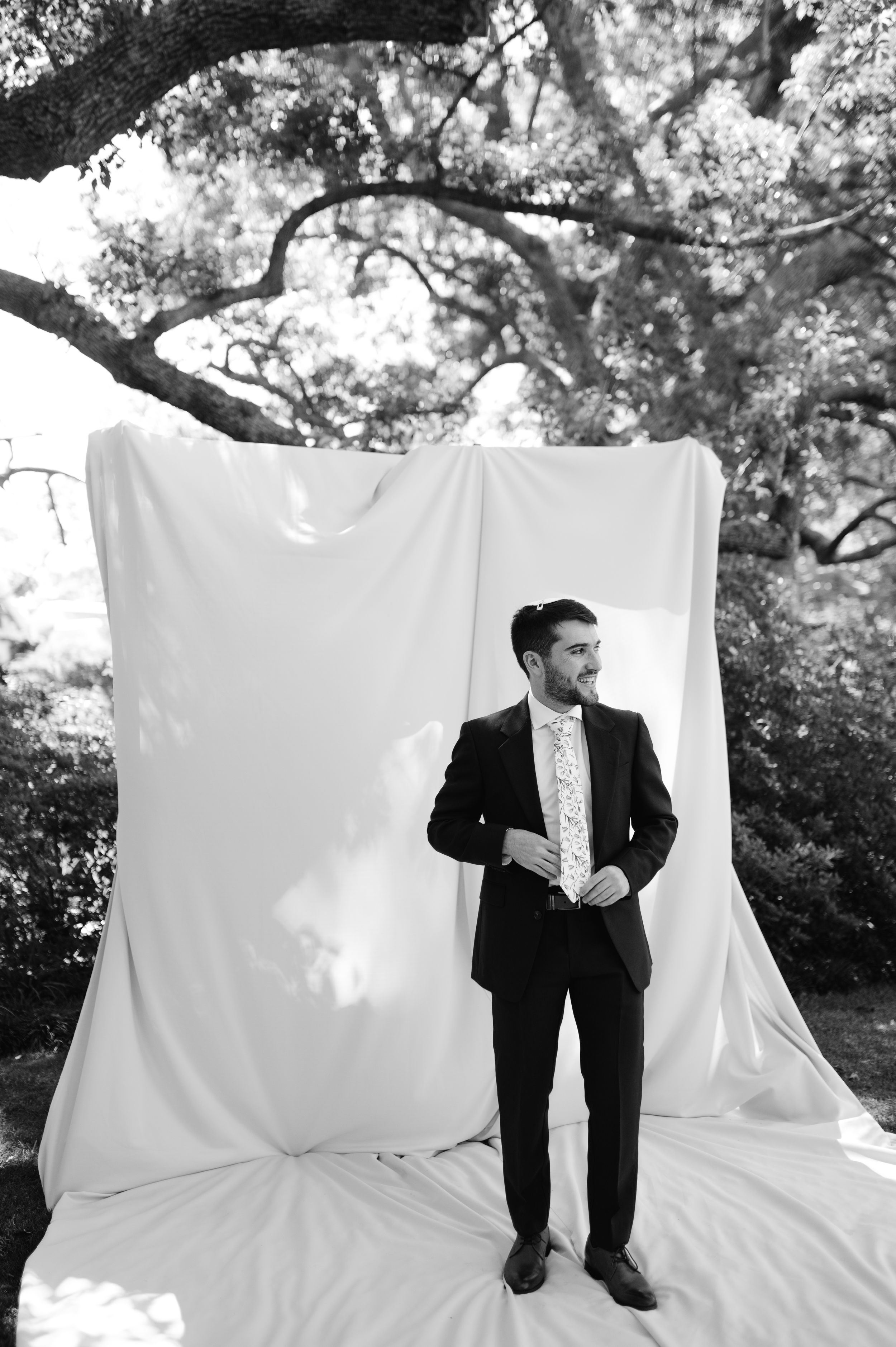 A sequence of black and white photos showing someone sitting on a white sheet or backdrop in a garden setting.
