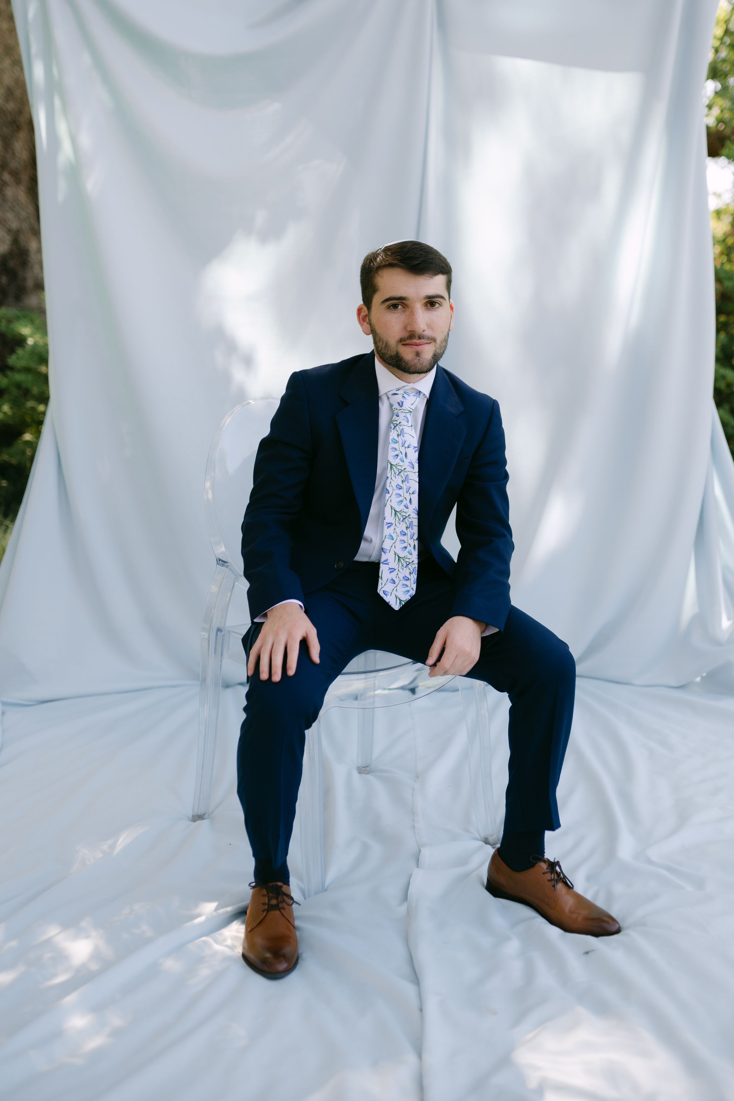 Formal portrait series on white backdrop showing person in navy suit and patterned tie sitting in different poses.