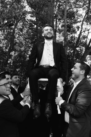 A sequence of black and white photos showing men in suits celebrating joyfully at an outdoor gathering.